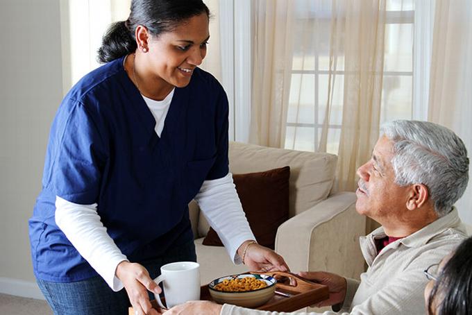 Indian care worker serving food to elderly man